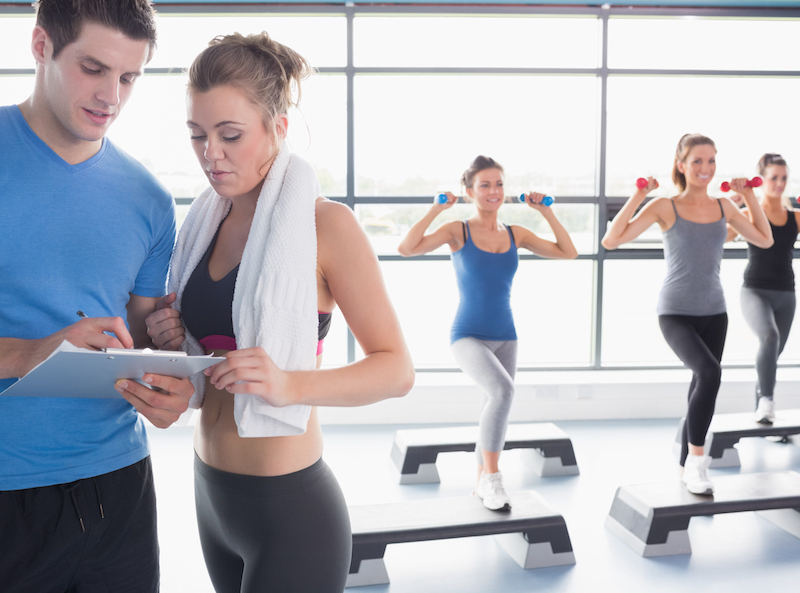 Women doing aerobics while trainer talking to woman in gym
